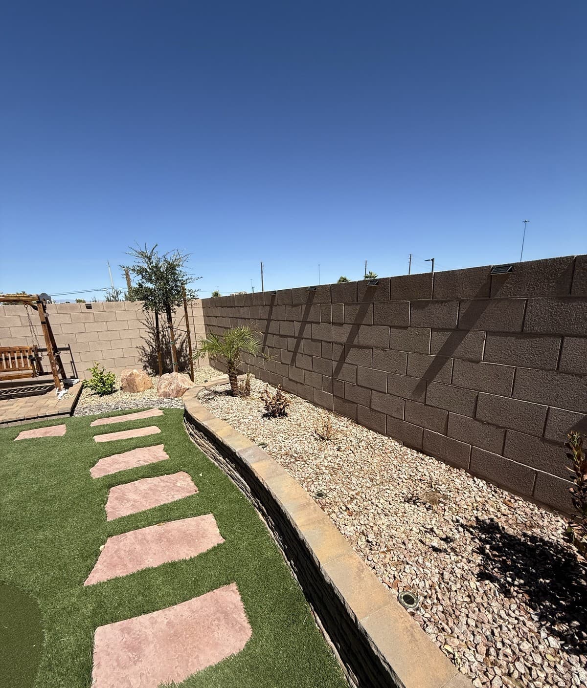 New desert plantings and gravel along the back wall of a turf and stepping-stone backyard, Las Vegas