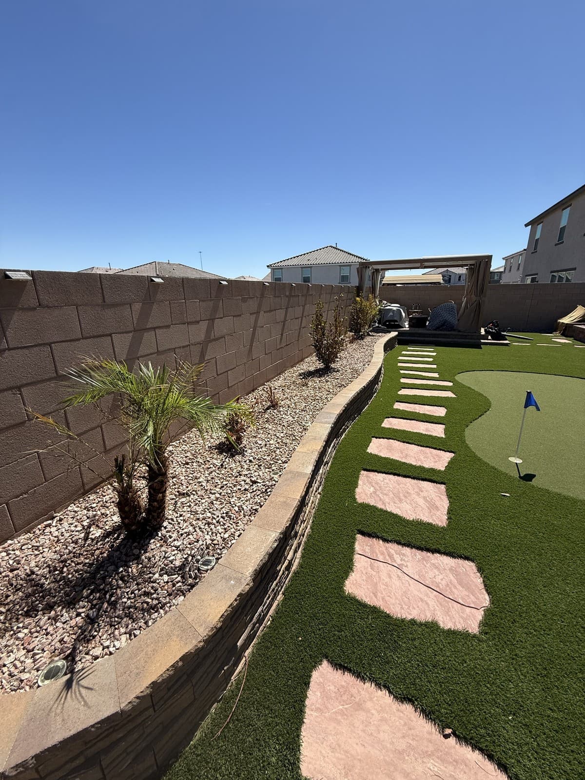 A backyard artificial turf putting green and stepping-stone path bordered by new palms and a gravel planting bed, Las Vegas